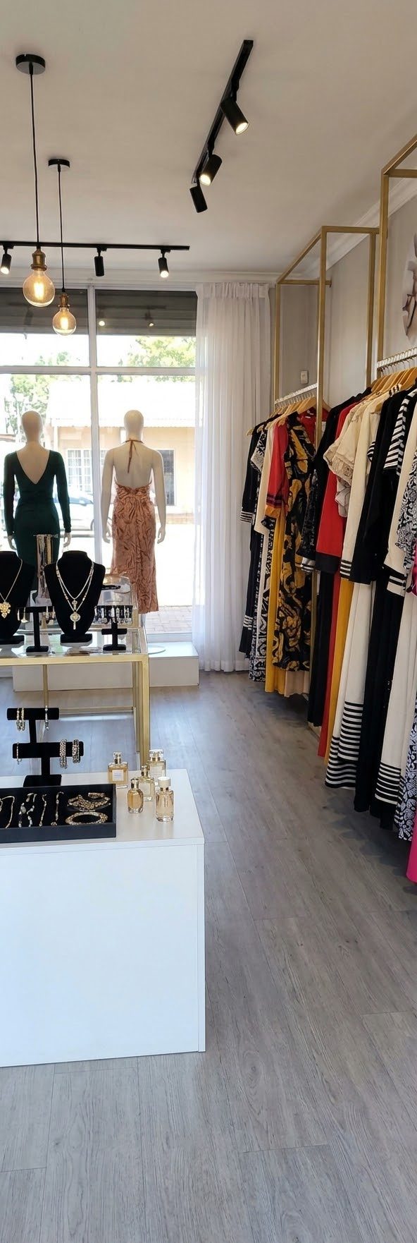 Inside a clothing boutique with track lighting, a window and a rail of clothes